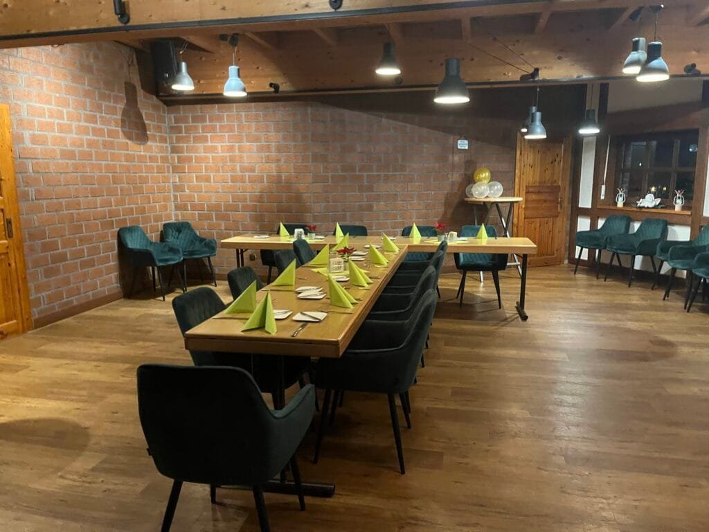 Bestuhlter Eventraum der Tenne mit U-förmiger Tafel, grünen Servietten, Ziegelwand und Holzdecke.
