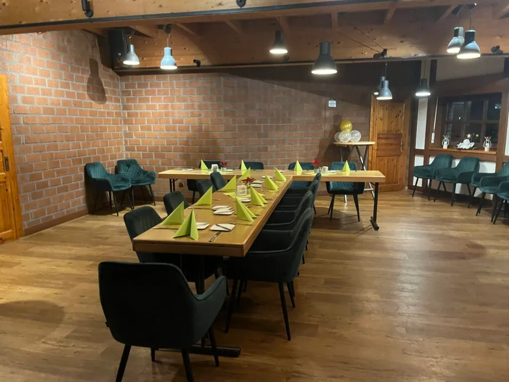 Bestuhlter Eventraum der Tenne mit U-förmiger Tafel, grünen Servietten, Ziegelwand und Holzdecke.